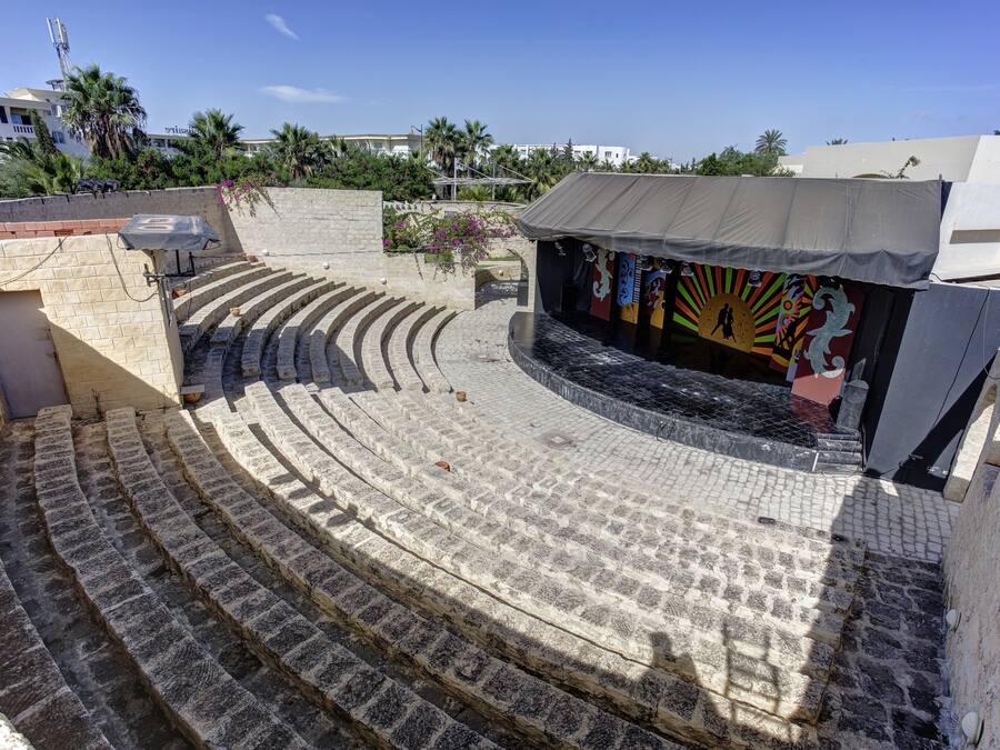 Un anfiteatro al aire libre con gradas de piedra y un escenario con telones de fondo coloridos.