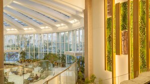 Un amplio atrio con techo de vidrio, una escalera central y un área de descanso con plantas.