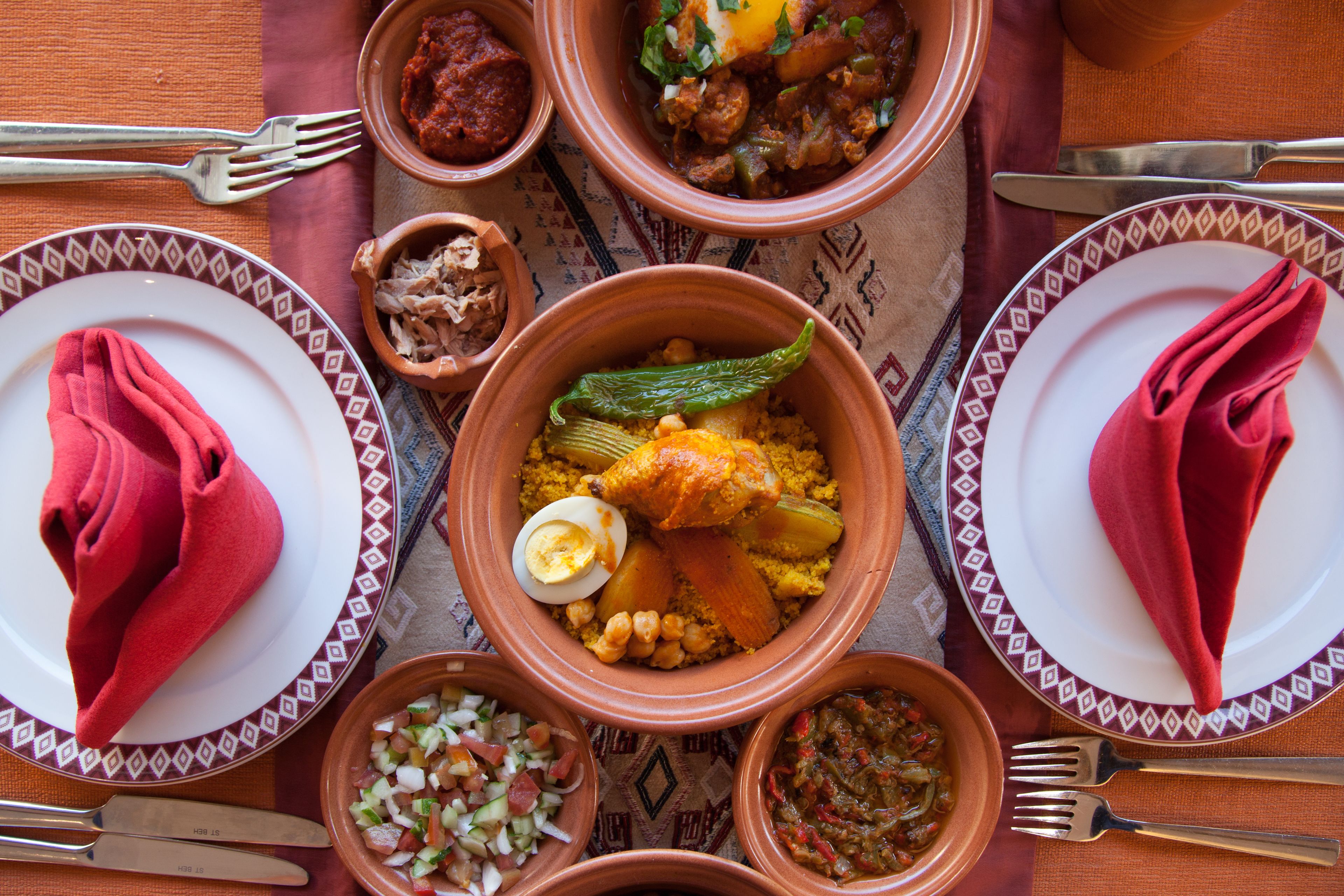 Une table dressée avec de nombreux plats, notamment un plat de couscous, un plat de ragoût et un saladier.