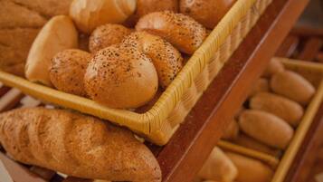 Un panier à pain en bois, rempli de différents types de pain, notamment des petits pains et des baguettes, posé sur une surface en bois.