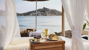 A beachside dining setup with a table, plates of food, a drink, and a view of the sea and a mountain. - TUI MAGIC LIFE Sarigerme - All Inclusive (Ortaca)