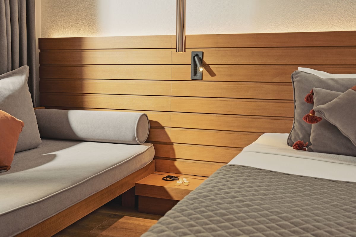 Ein modernes Schlafzimmer mit einem Holzkopfteil, einer Couch, einem Bett mit gesteppter Bettdecke und einem Nachttisch mit Lampe.