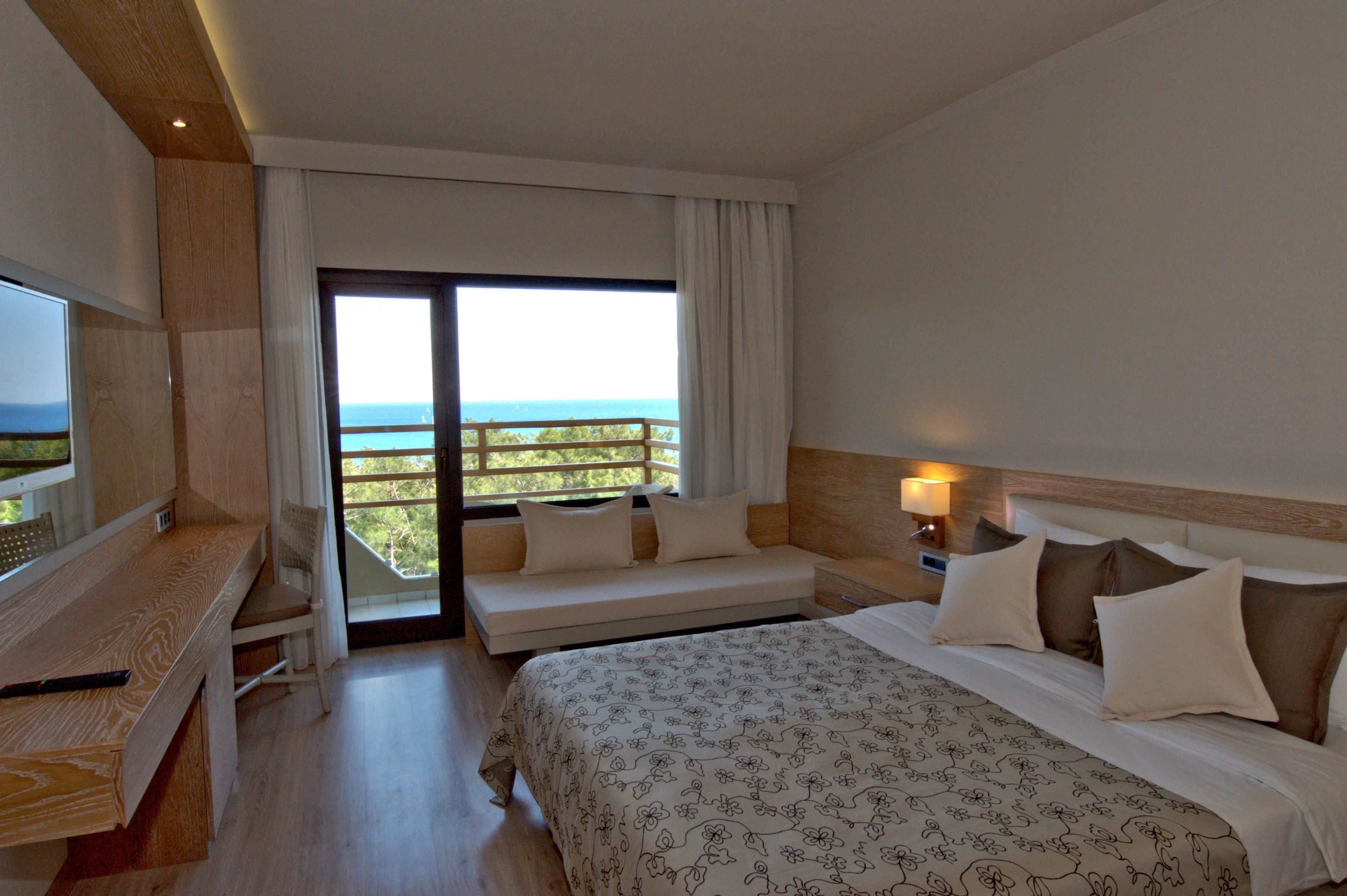 Ein Hotelzimmer mit Bett, Schreibtisch, Stuhl, Sofa, Fernseher und einem Balkon mit Aussicht.