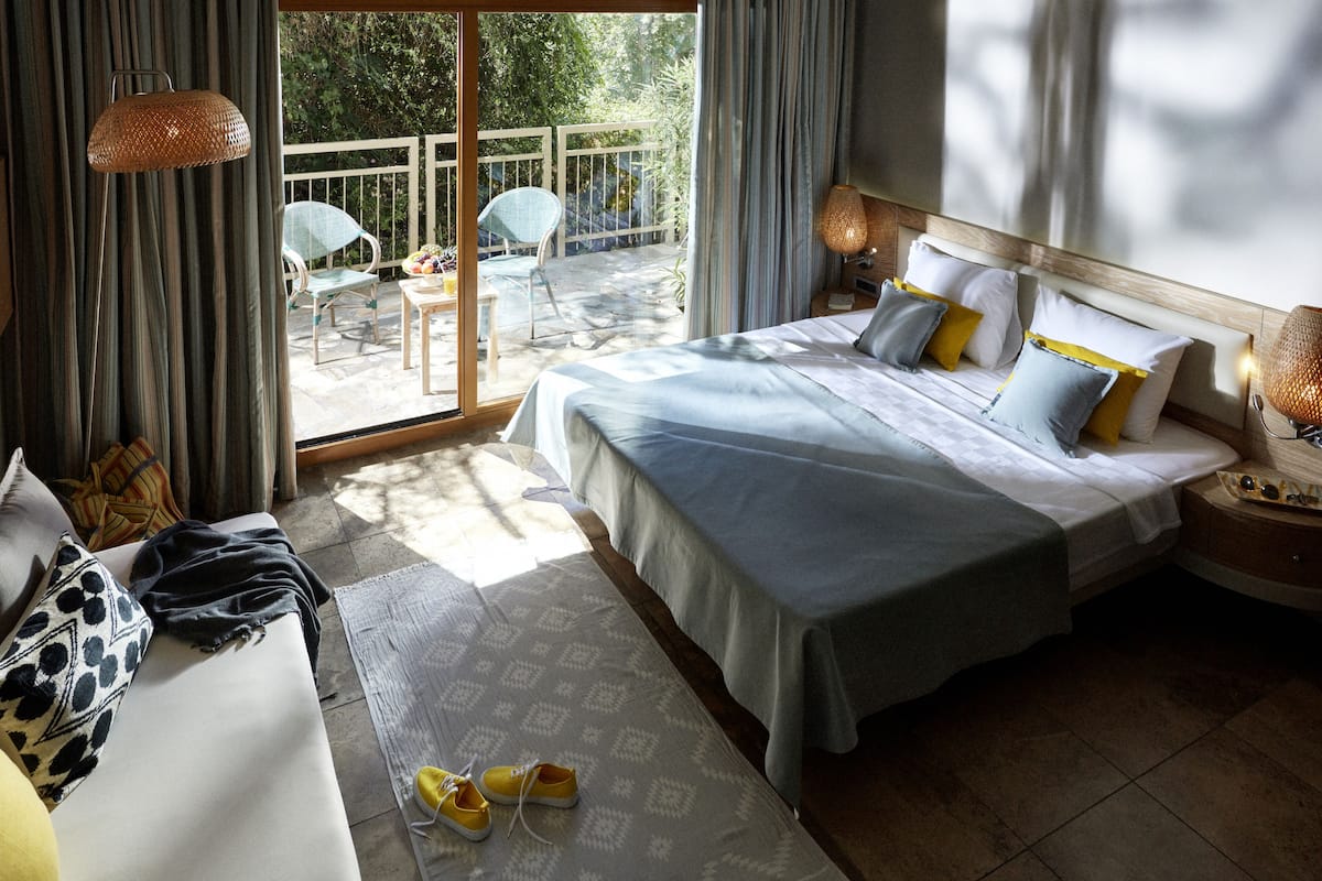 Ein Hotelzimmer mit einem großen Bett, einer Couch, einem Balkon mit Sitzgelegenheiten und Blick auf eine grüne Landschaft.