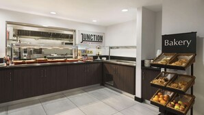 Cozinha moderna com armários escuros, bancada de aço inoxidável e vitrine para produtos de panificação.