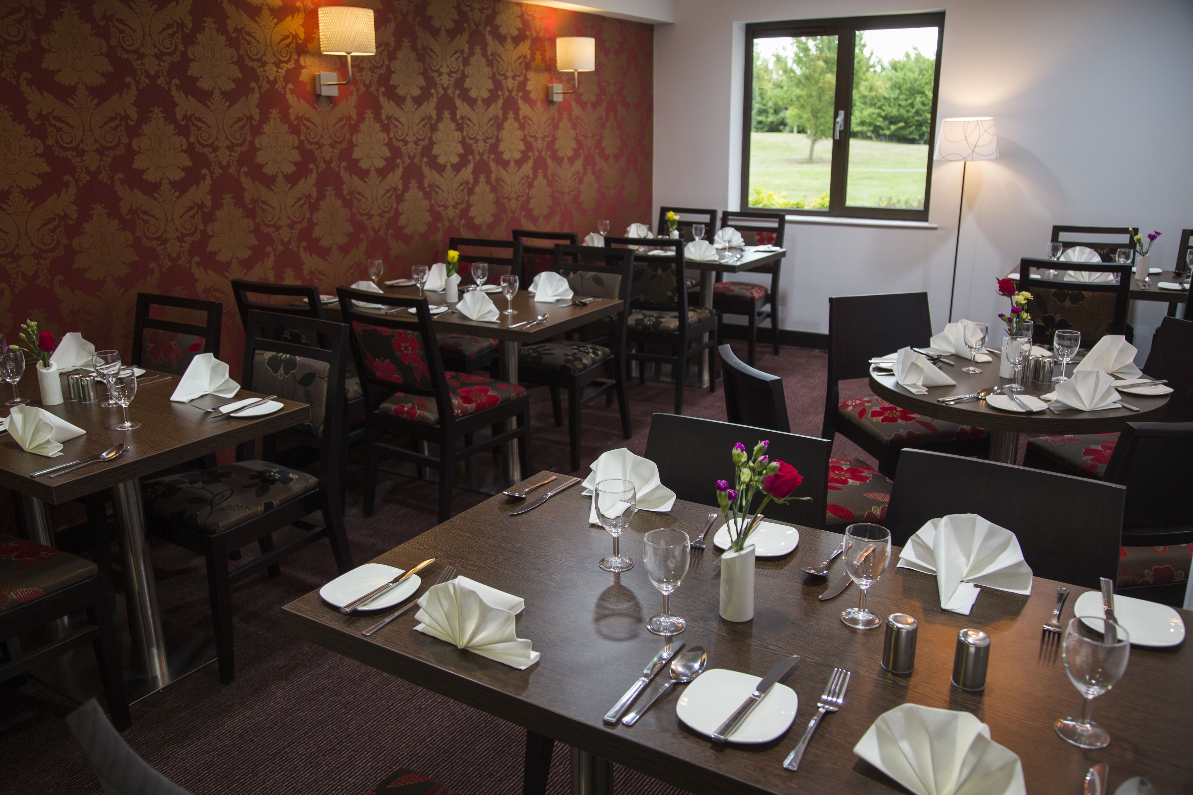 Comedor con mesas dispuestas para varios comensales, con sillas, vajilla y detalles decorativos.