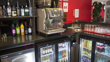 Un área de bar con una máquina de café, estantes con diversas bebidas y dos refrigeradores llenos de productos.