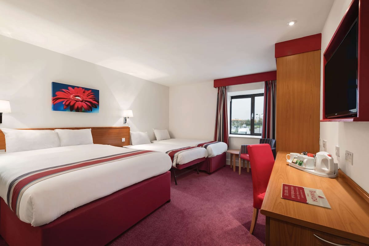 A hotel room with two beds, a desk, a chair, a TV, a window with curtains, and a red flower painting on the wall.