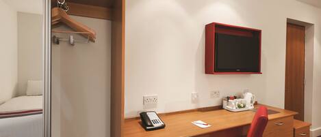 A hotel room with a wooden desk, a red chair, a telephone, and a television mounted on the wall.