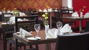 Un espace repas avec des tables mises pour le service, comprenant des verres à vin, des serviettes et un vase avec des fleurs.