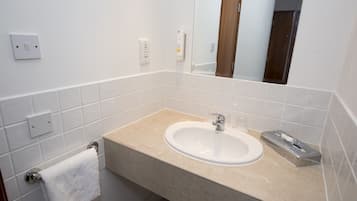 Un baño con un lavabo color crema, baldosas blancas, un perchero, un espejo y un secador de manos.