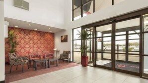Um saguão de hotel com parede estampada, área de estar e grandes portas de vidro que dão para o exterior.