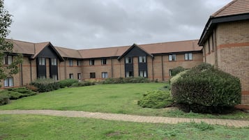 A multi-story building with a brick facade, a central courtyard with a lawn, and a brick pathway leading to the entrance.