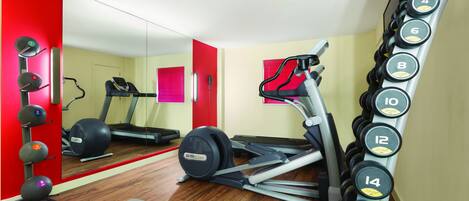 A gym with exercise equipment, a treadmill, and a mirror reflecting the room.