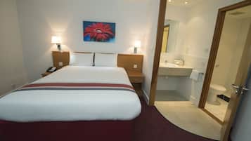 A hotel room with a large bed, bedside lamps, a painting on the wall, and a bathroom visible through an open door.