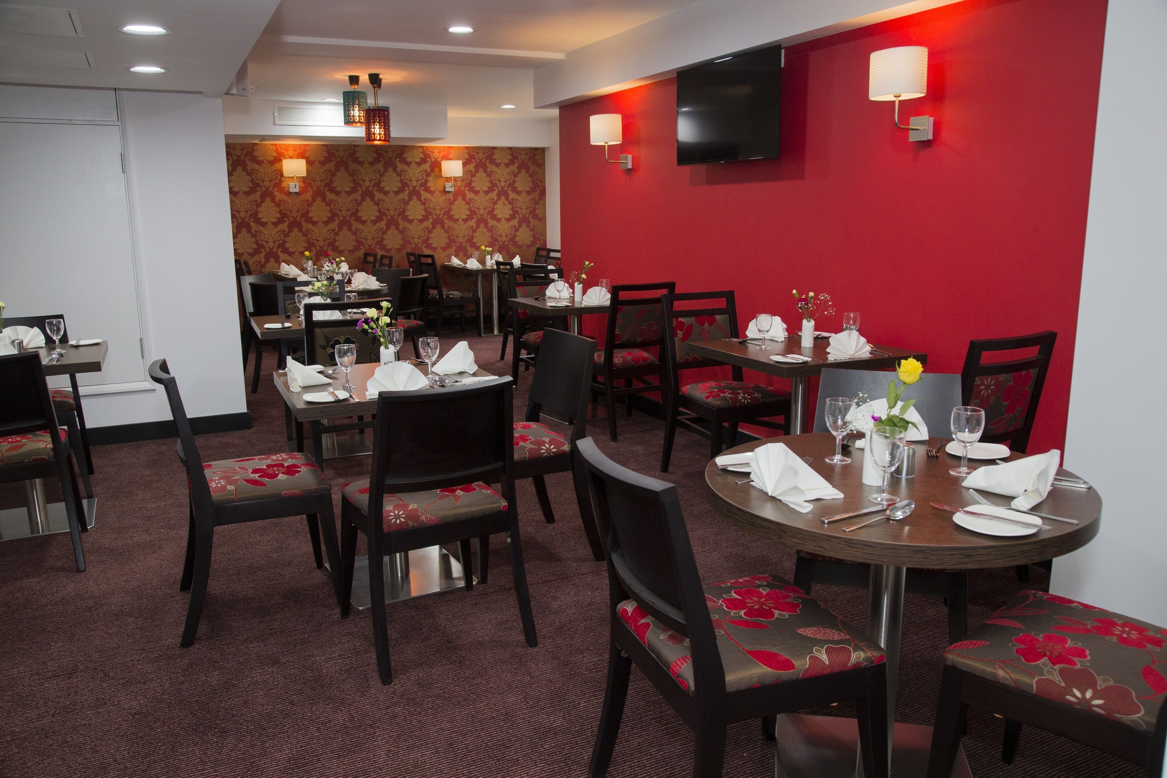 Une salle à manger d’hôtel avec des tables rondes, des chaises et des murs rouges.