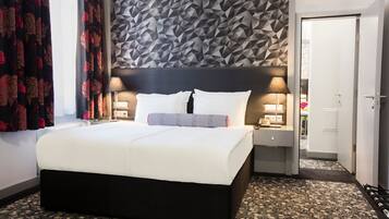 Ein modernes Hotelzimmer mit einem großen Bett, geometrischem Wanddesign und zwei Nachttischlampen.