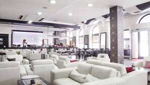 A spacious lounge area with white leather sofas, a bar area with a bartender, and large windows providing natural light. - Hotel Central (Sarajevo)