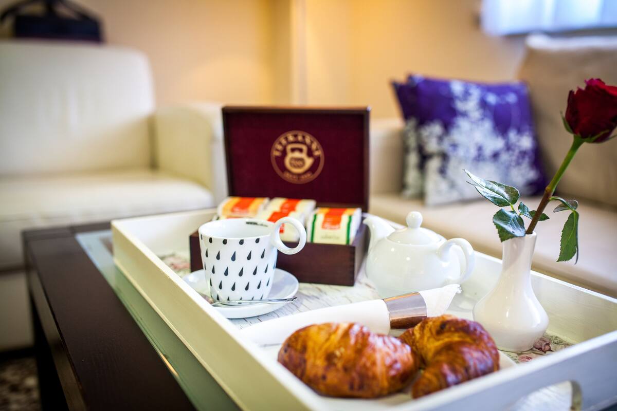 Una bandeja con croissants, una tetera, una taza y una caja de té sobre una mesa en un salón.