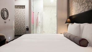 A hotel room with a large bed, a glass shower door, a round mirror, and a patterned wall. - Hotel Central (Sarajevo)