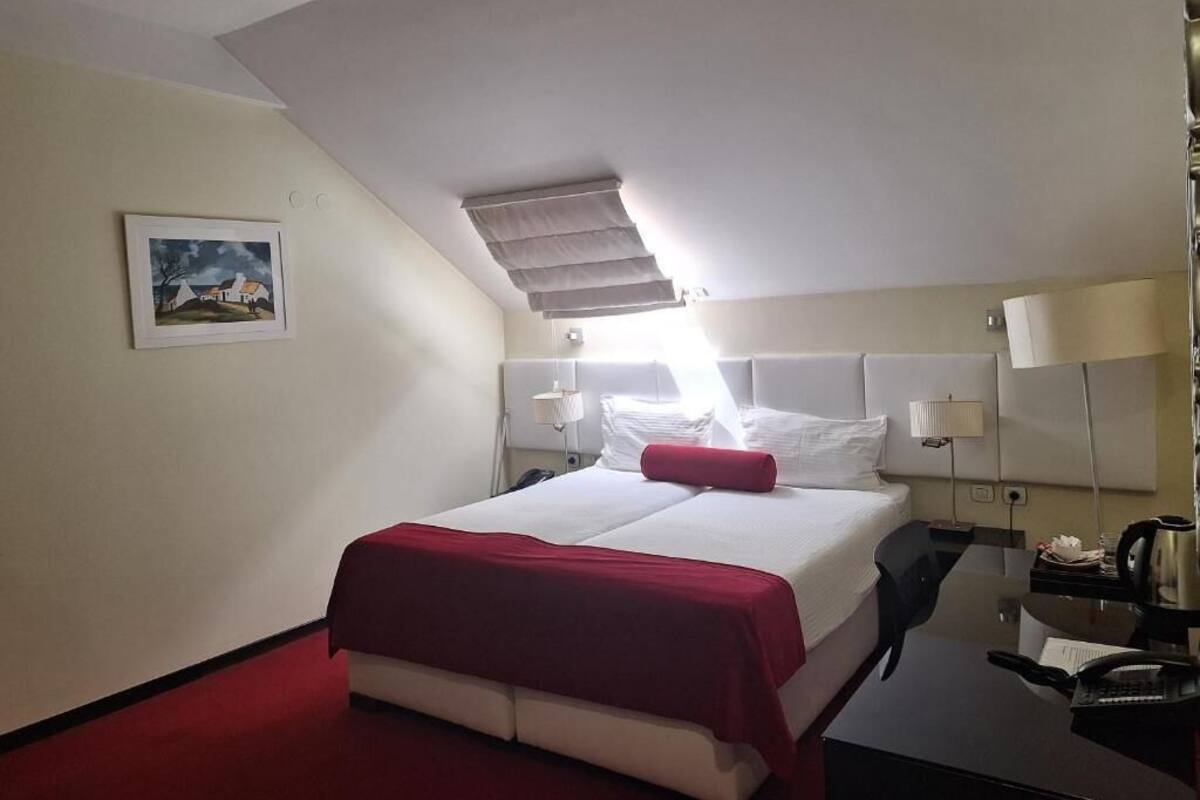 Una habitación de hotel con cama, escritorio, lámpara y un cuadro en la pared.