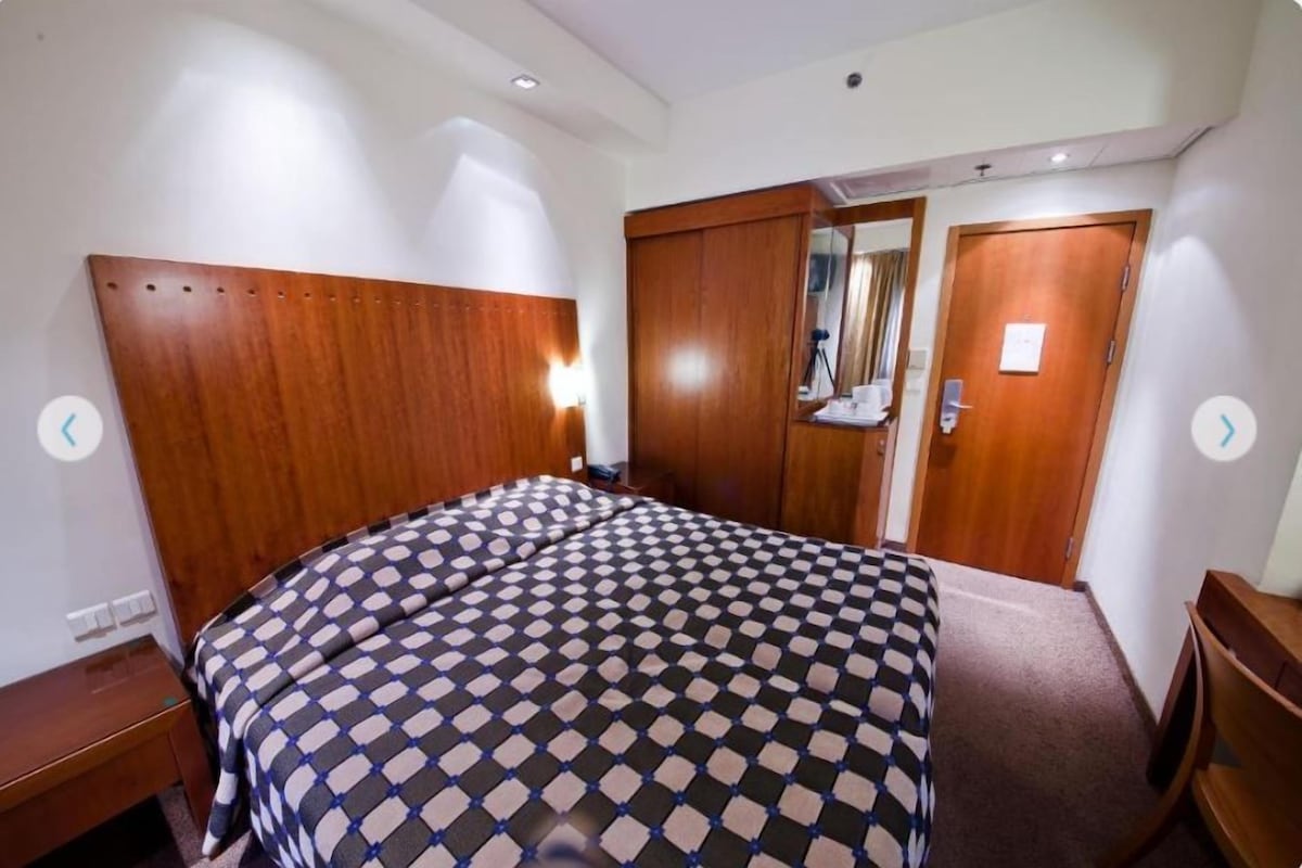Una habitación de hotel con cabecera de madera, colcha a cuadros, armario de madera y un espejo.