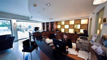 A reception desk with a receptionist, a large window, and a plant in the background.