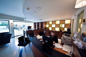 A reception desk with a receptionist, a large window, and a plant in the background.