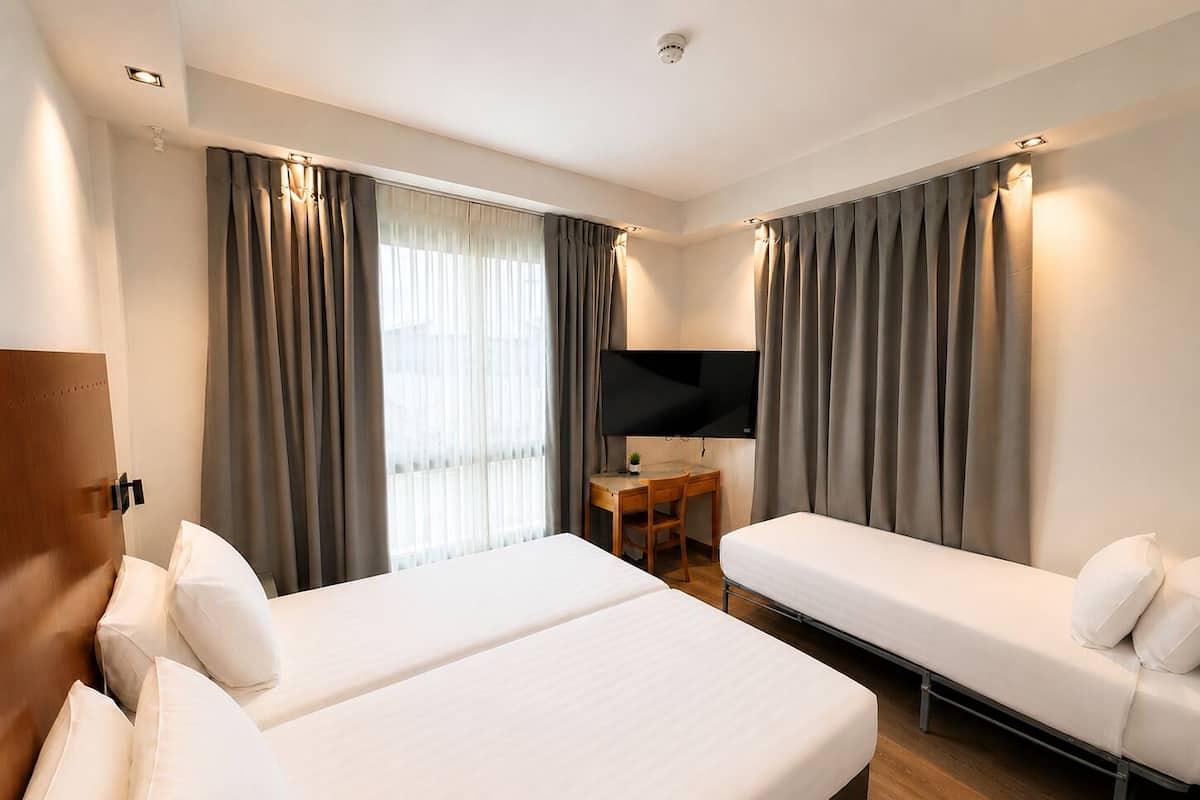 A hotel room with two beds, a desk, a TV, and curtains.