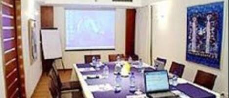 A conference room with a long table, chairs, a projector, and a screen.