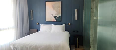 A bedroom with a large bed, a headboard, a bedside table, a lamp, and a painting on the wall.