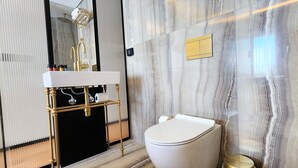 Un baño moderno con pared de mármol, lavamanos con marco dorado y retrete.