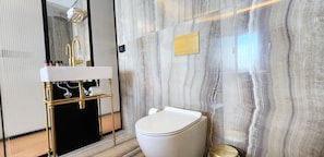 Un baño moderno con pared de mármol, lavamanos con marco dorado y retrete.