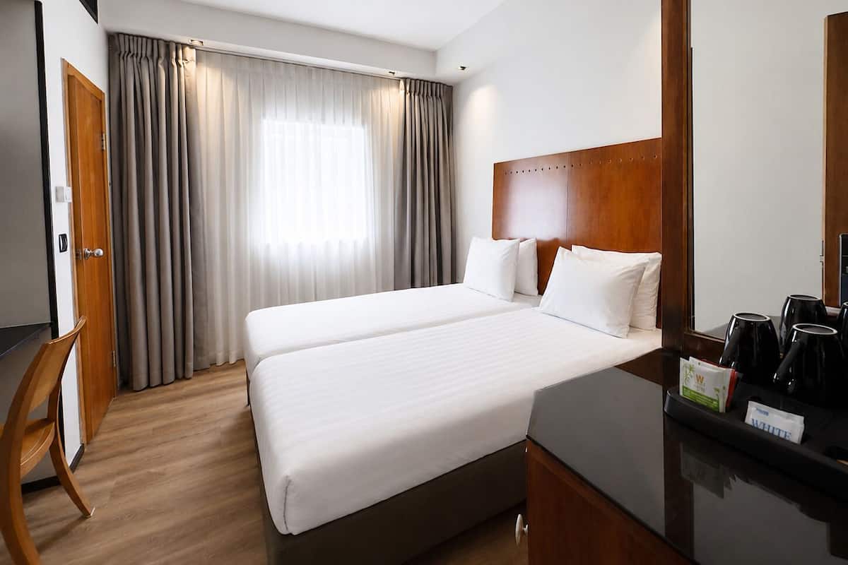 A hotel room with a double bed, a wooden headboard, a desk with a coffee machine, and a window with curtains.