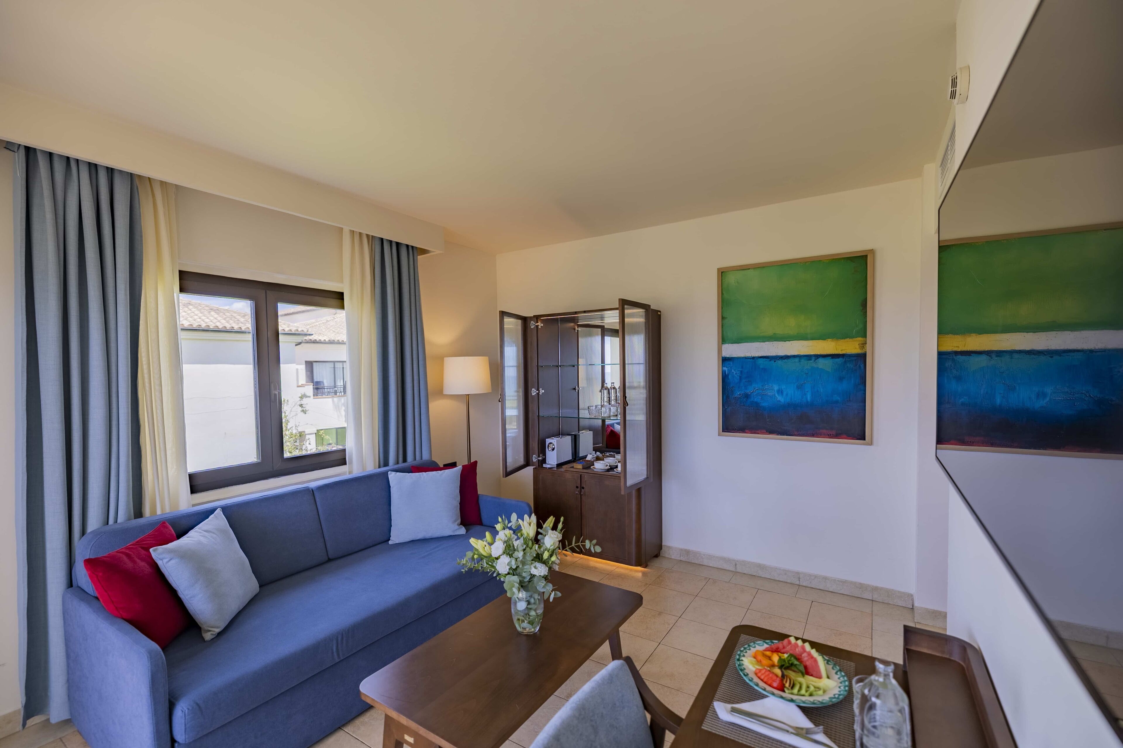 Una habitación de hotel moderna con un sofá azul, una mesa de comedor con un florero y un mueble con microondas.