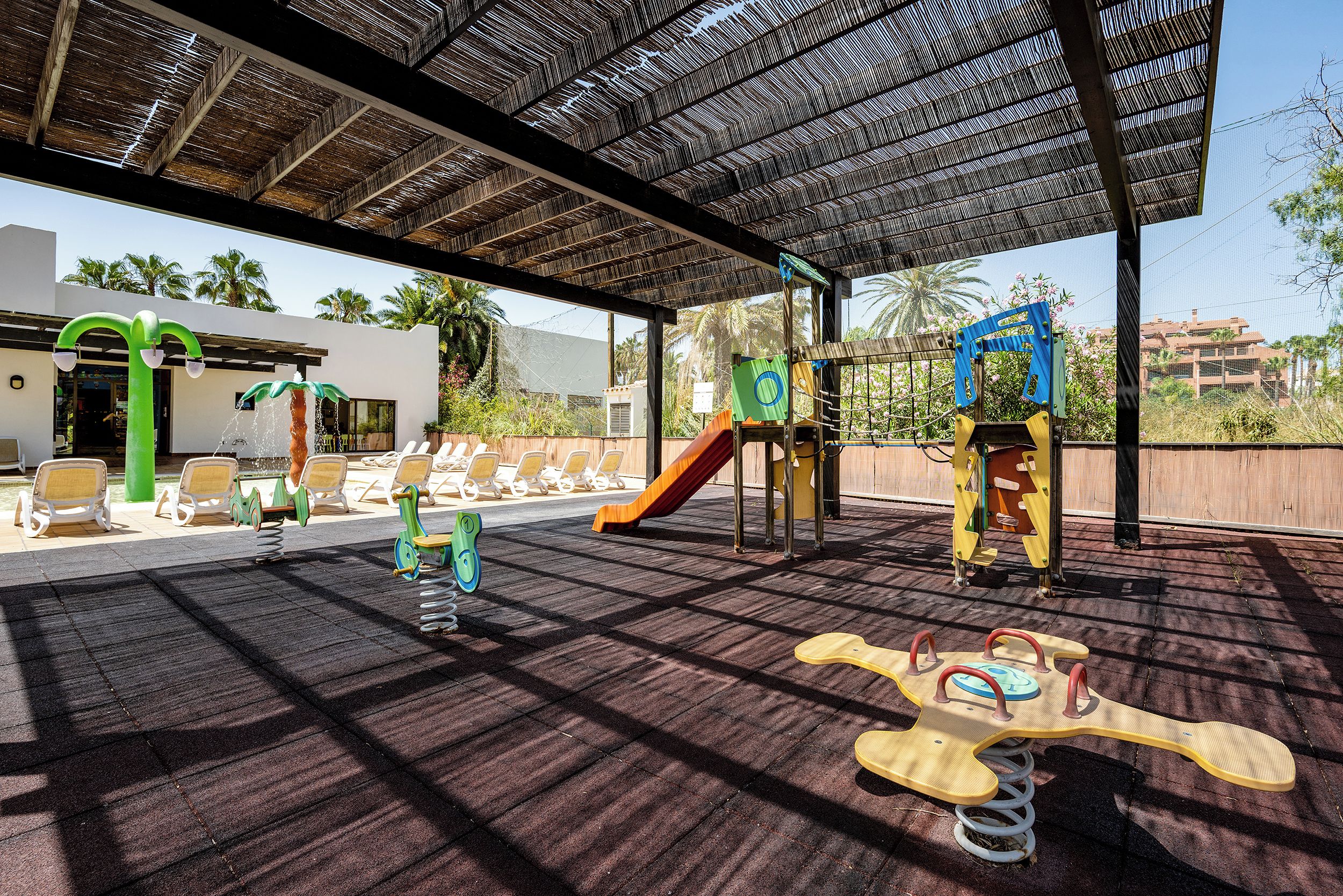 Un área de juegos al aire libre con diversas estructuras, incluyendo un tobogán, columpios y un balancín.