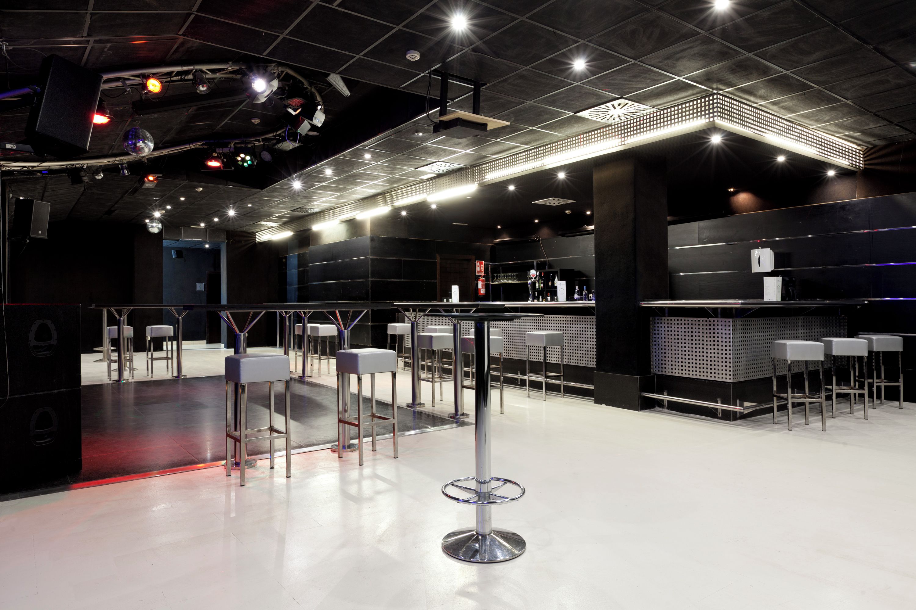 Un área de bar moderna con taburetes altos, una barra y luces colgantes.