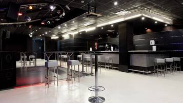 Un área de bar moderna con taburetes altos, una barra y luces colgantes.