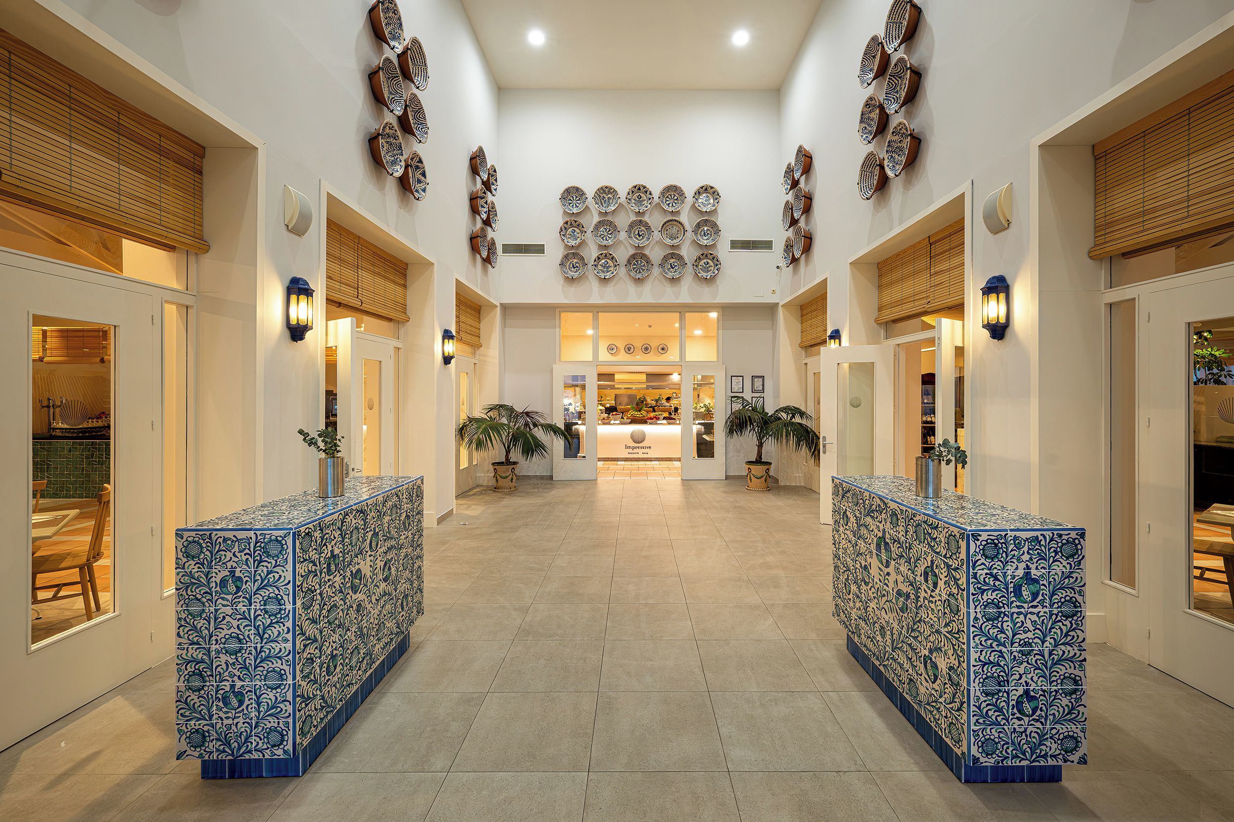 Un vestíbulo de hotel con una recepción central, paneles decorativos en la pared y plantas en macetas.
