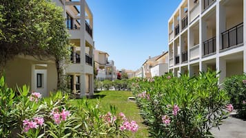 A residential building with balconies, a clear sky, and a garden with pink flowers.