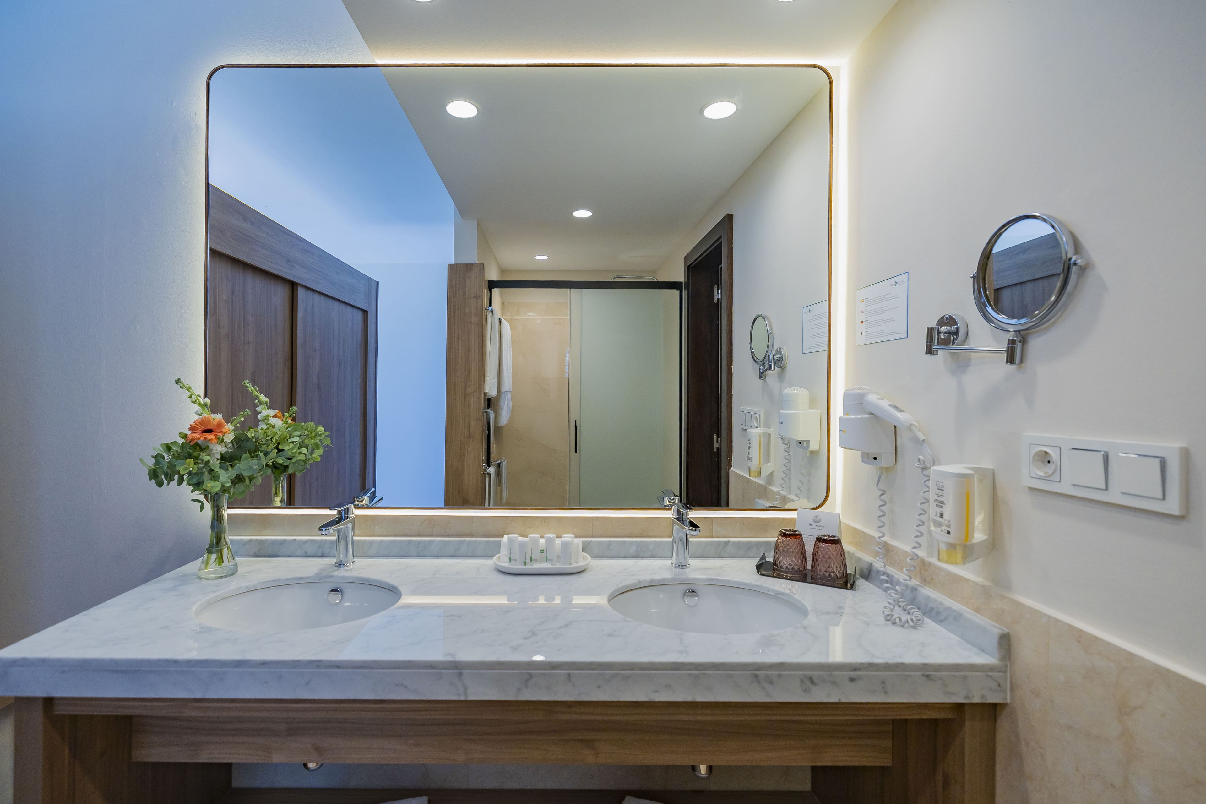 A modern bathroom with two sinks, a large mirror, and a wooden vanity.