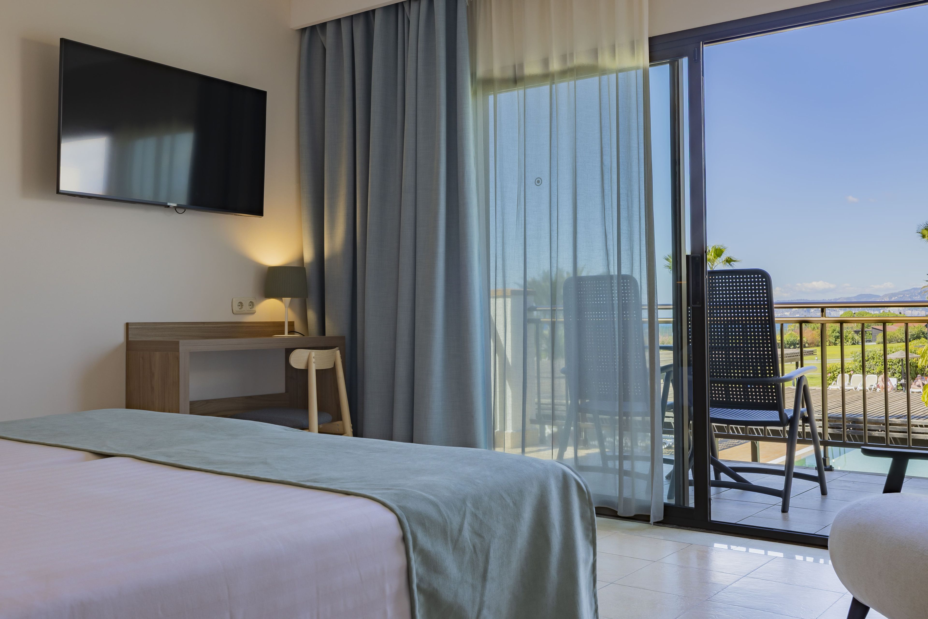 Une chambre d’hôtel avec un lit, un bureau, une chaise, une télévision et un balcon avec vue.