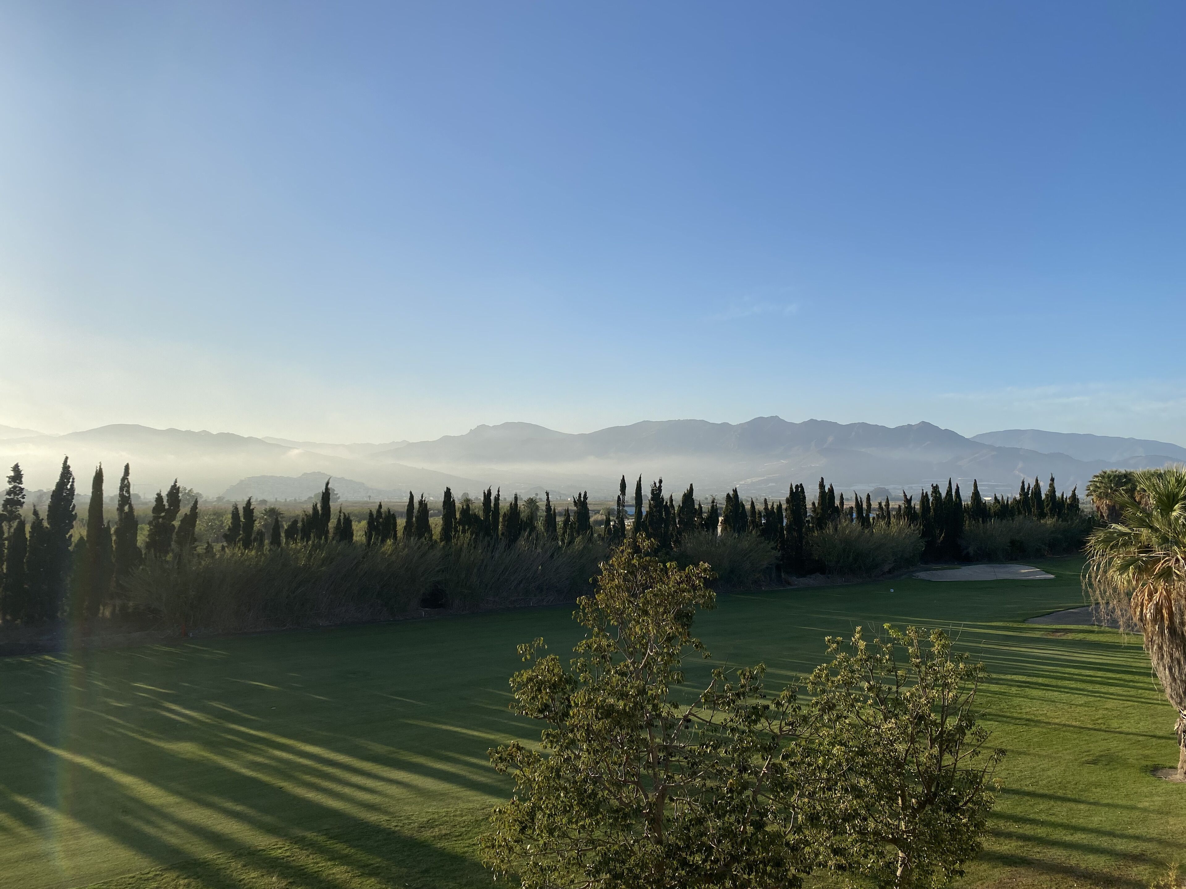 Campo de golf con vista despejada a montañas distantes y un horizonte brumoso.
