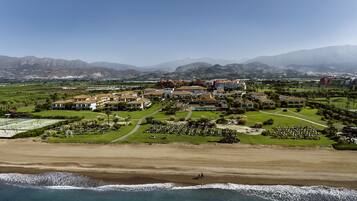 An aerial view of a coastal resort with multiple buildings, a golf course, and a beach.