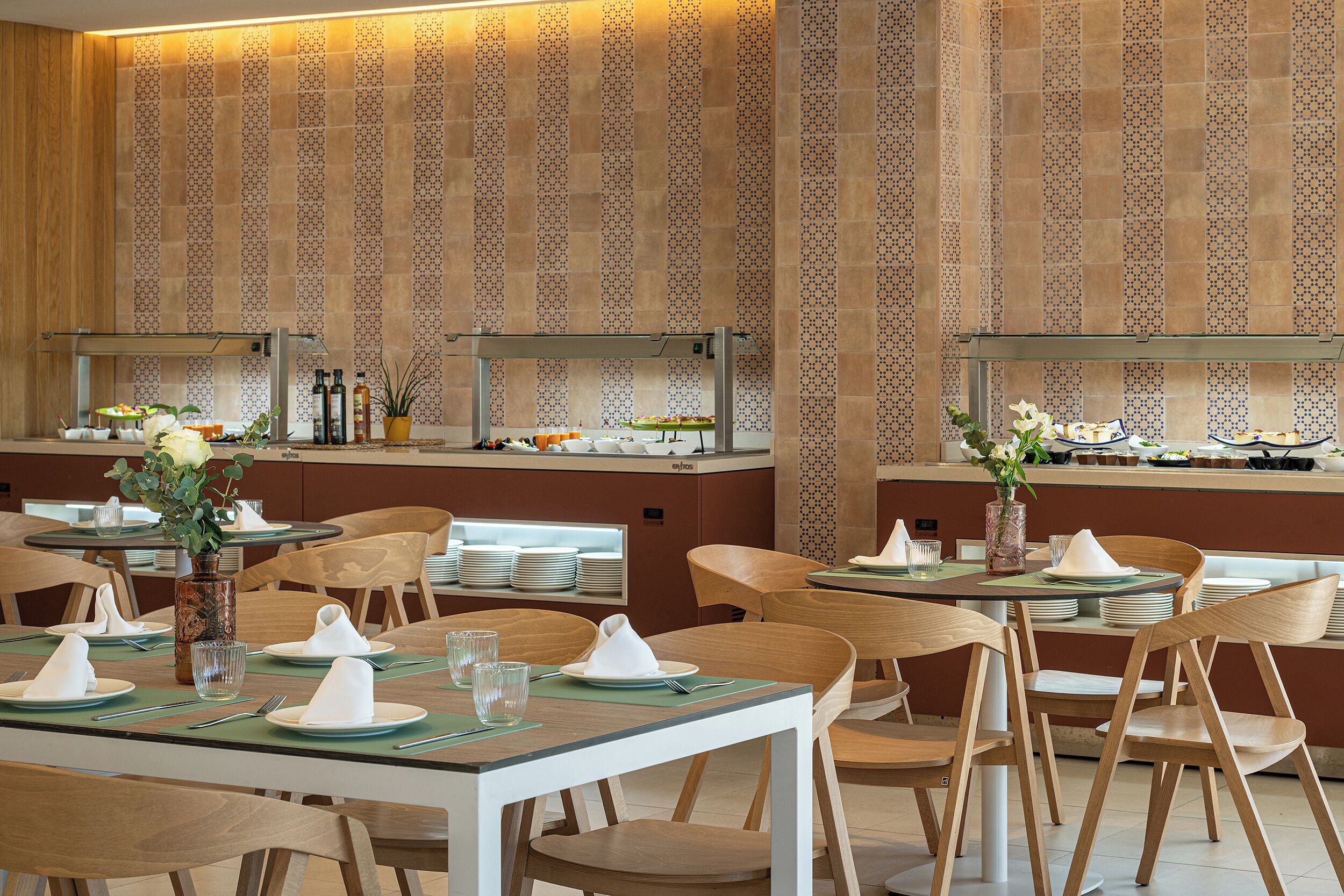 Un restaurante con varias mesas y sillas, un muro con diseño y una barra con productos alimenticios.