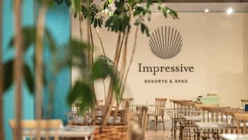 L’intérieur d’un restaurant, avec une enseigne indiquant « Impressive Resorts & Spas » et un logo stylisé en forme de coquillage. Des tables et des chaises sont disposées pour accueillir les clients.