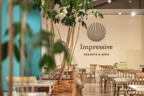 A restaurant interior with a sign reading 'Impressive Resorts & Spas' and a stylized shell logo. Tables and chairs are arranged for dining. - Impressive Playa Granada Golf (Motril)