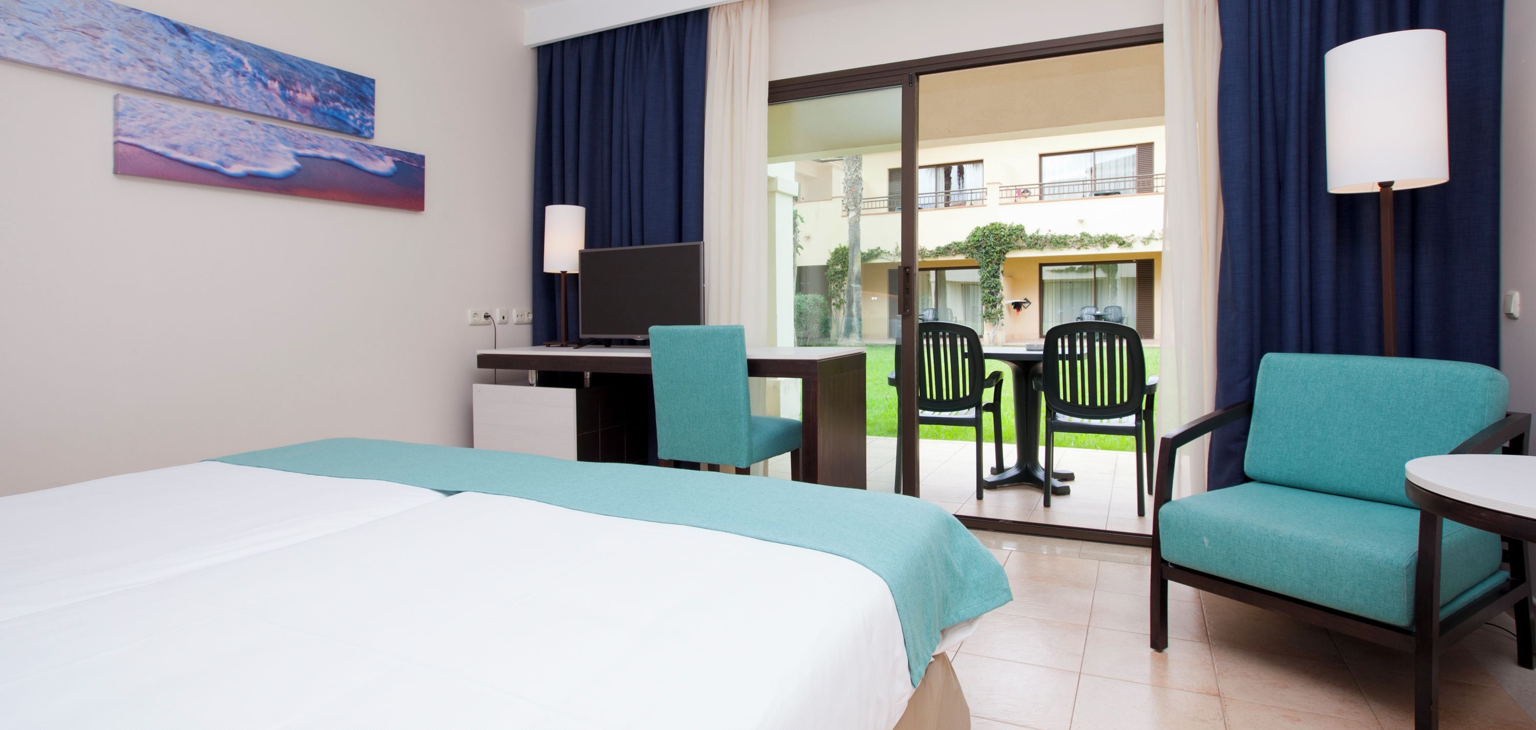 Une chambre d’hôtel comprenant un lit, un bureau, deux chaises, une table et donnant sur l’espace extérieur.