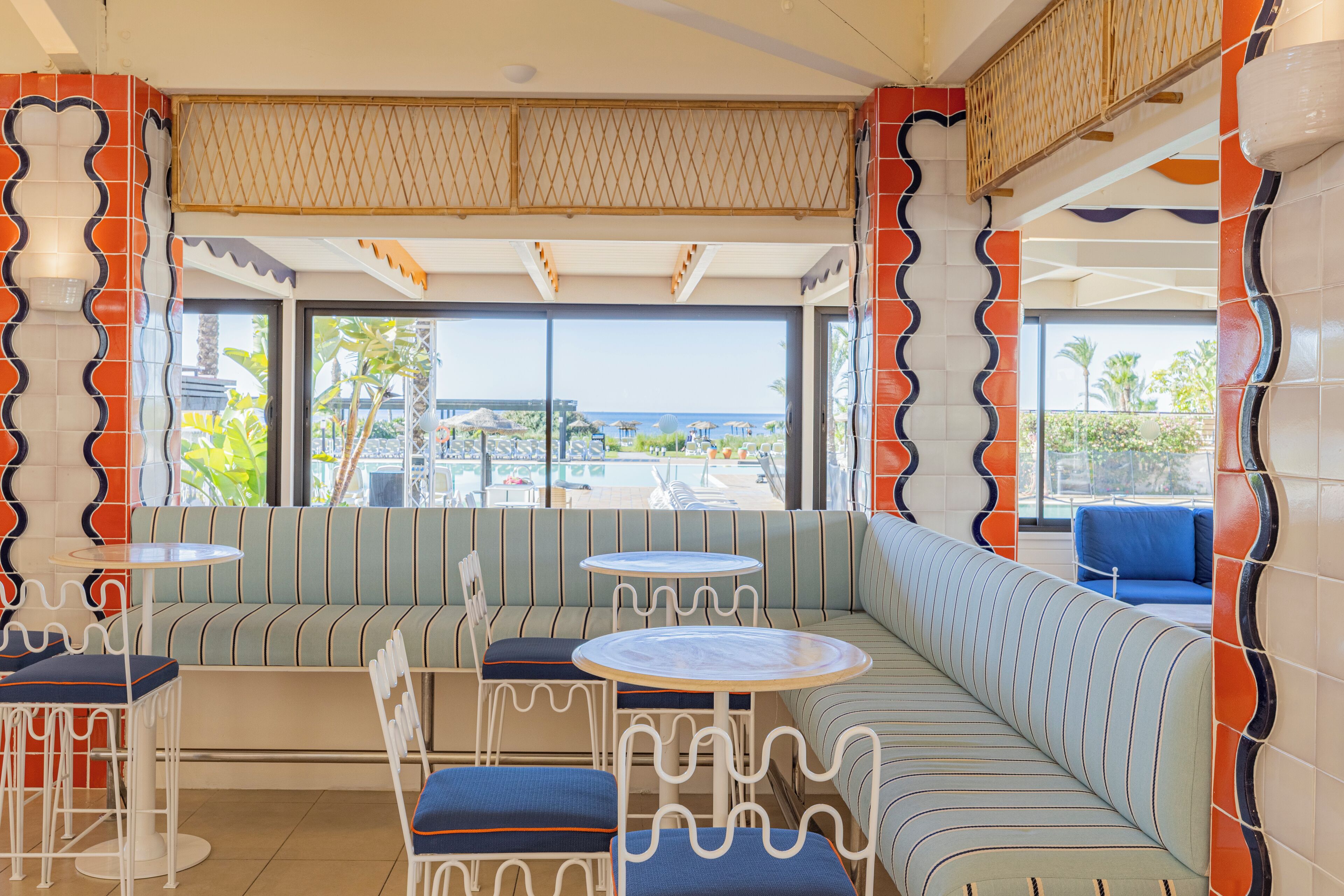 Een moderne lounge met een groot raam, gestreepte zitplaatsen en ronde tafels.
