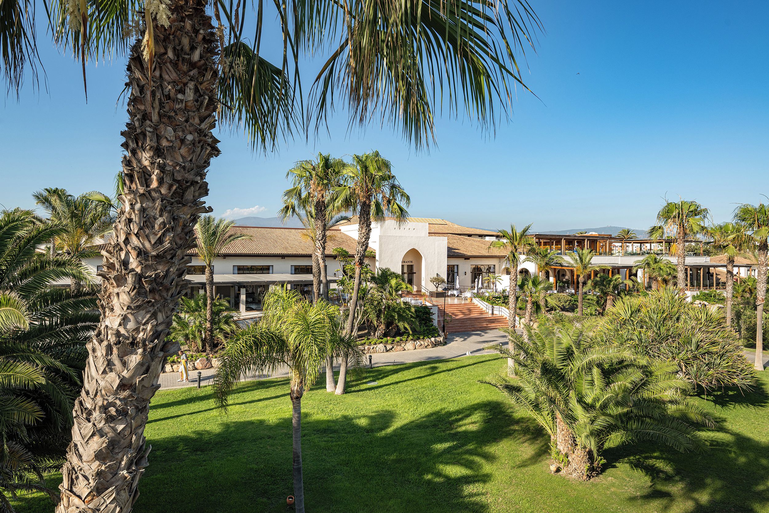 Un resort con palmeras, piscina y un edificio de techo de tejas.